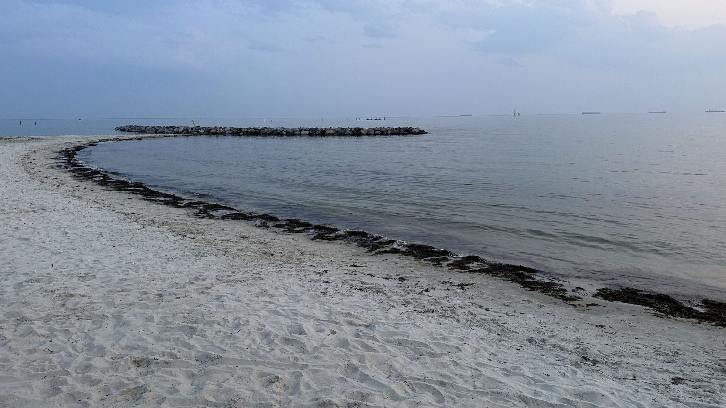 Sandy Chesapeake Bay shoreline with a rock jetty under a hazy evening sky